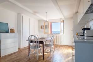 A dining area with a wooden table and chairs, a white cabinet, a radiator, and a window with a view. - LA HAUT - Center annecy- Balcony view lake (Annecy)