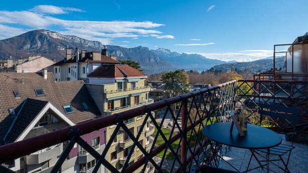 A balcony with a table and chairs, overlooking a mountainous landscape with buildings in the foreground. - Studio Gatsby - Center Annecy - Balcony view lake (Annecy)