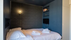 A modern bedroom with a geometric-patterned headboard, a flat-screen TV, and neatly folded towels on the bed. - Studio Gatsby - Center Annecy - Balcony view lake (Annecy)
