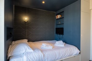 Ein modernes Schlafzimmer mit einem Kopfteil im geometrischen Muster, einem Flachbildfernseher und ordentlich gefalteten Handtüchern auf dem Bett.