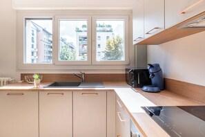 Eine moderne Küche mit Spüle, Mikrowelle und Herd. Fenster bieten Blick auf umliegende Gebäude.