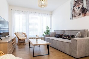 Ein Wohnzimmer mit einer Couch, einem Fernseher, einem Korbstuhl, einem Tisch und einer Pflanze.