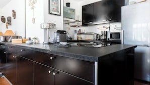 A modern kitchen with a large island, black cabinets, stainless steel appliances, and a flat-screen TV. - At the gates of the old town - 2 bedrooms - Garage - Terrace (Annecy)