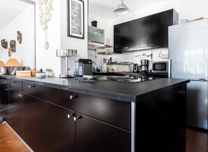 A modern kitchen with a large island, black cabinets, stainless steel appliances, and a flat-screen TV. - At the gates of the old town - 2 bedrooms - Garage - Terrace (Annecy)