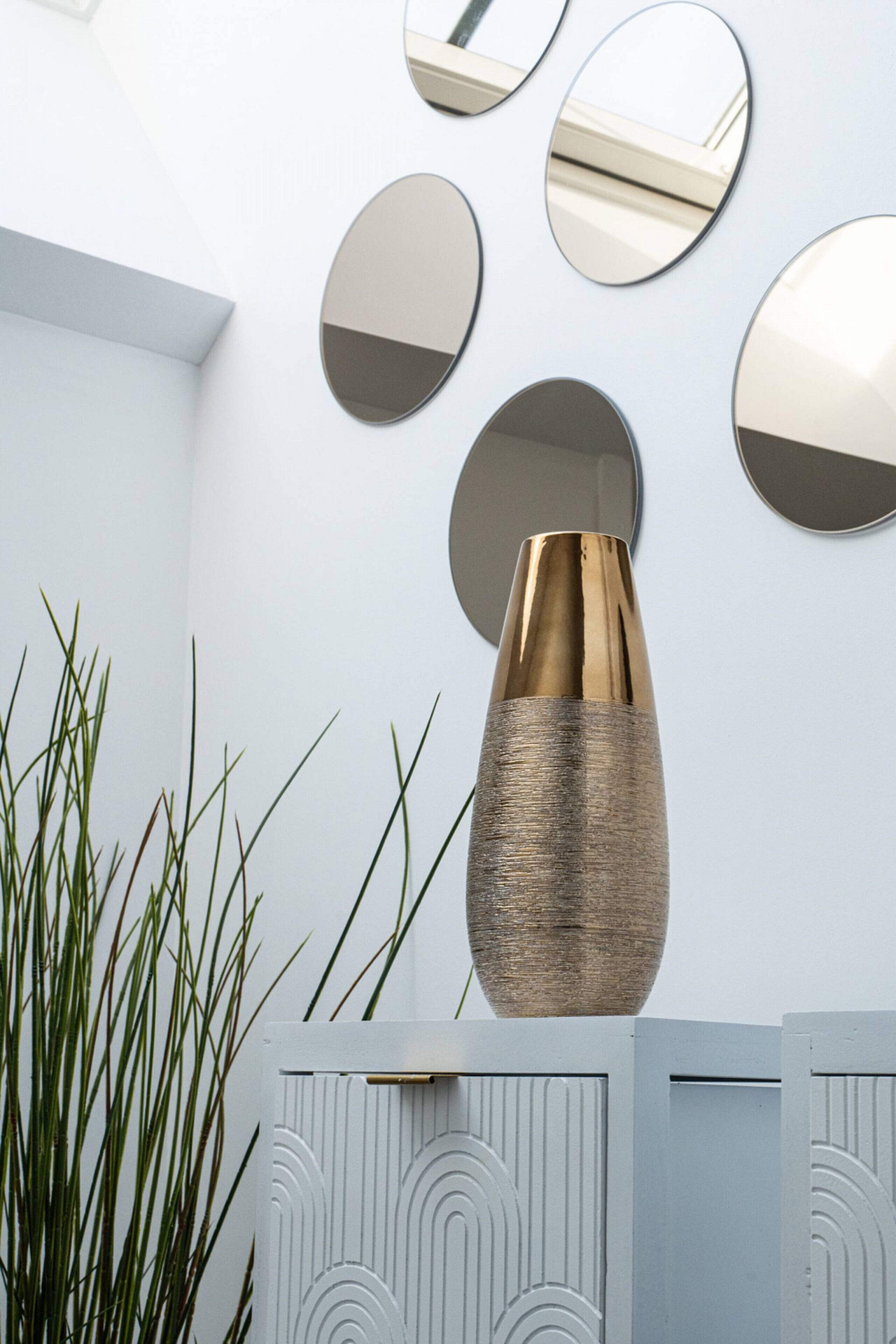 A modern interior with a decorative vase, wall-mounted mirrors, and a patterned cabinet.