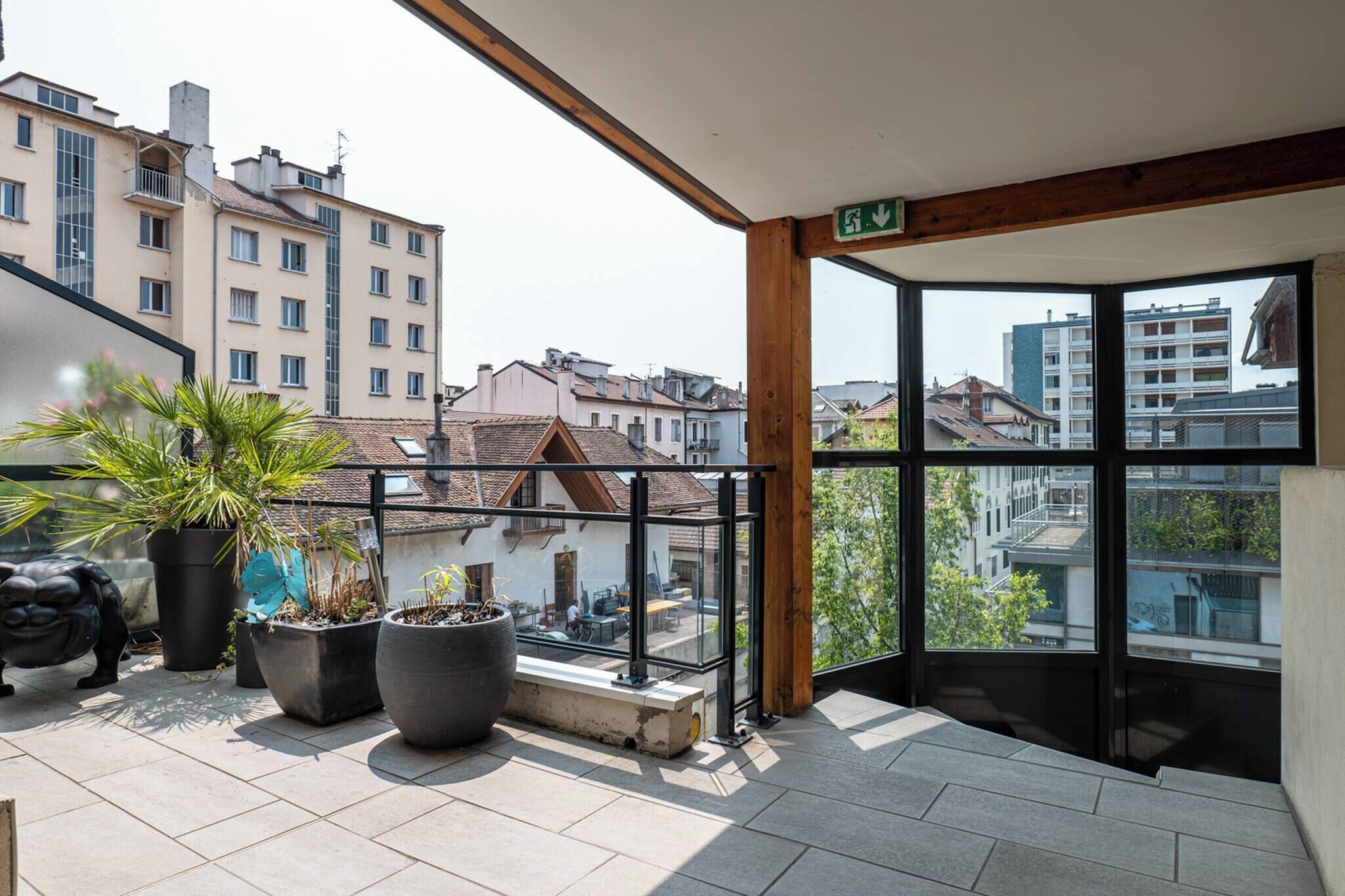 A balcony with potted plants, a bench, and a view of surrounding buildings.