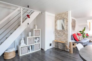 Eine Treppe mit weißer Geländer, ein weißer Beistelltisch mit Aufbewahrungsboxen, ein stachelkissenförmiger Sessel und ein graues Sofa mit roten Kissen.