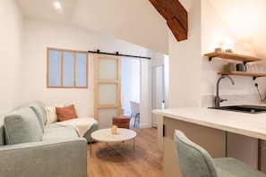Ein modernes Wohnzimmer mit einer Couch, einem Couchtisch und einer Küchenzeile mit Spüle und Regalen.