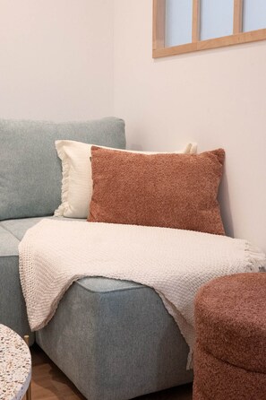 Ein Sofa mit einer hellgrauen und weißen Decke, einem braunen Kissen und einem kleinen runden Tisch mit einem Tischlein.