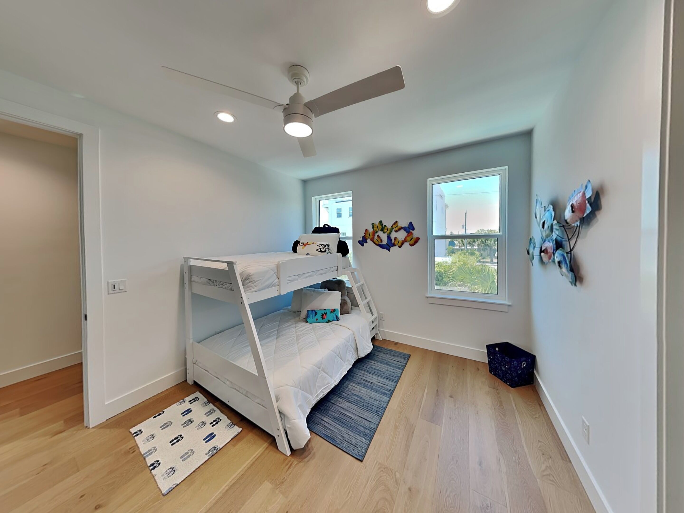 A room with a bunk bed, a ceiling fan, a window with a view, and a wall decoration.