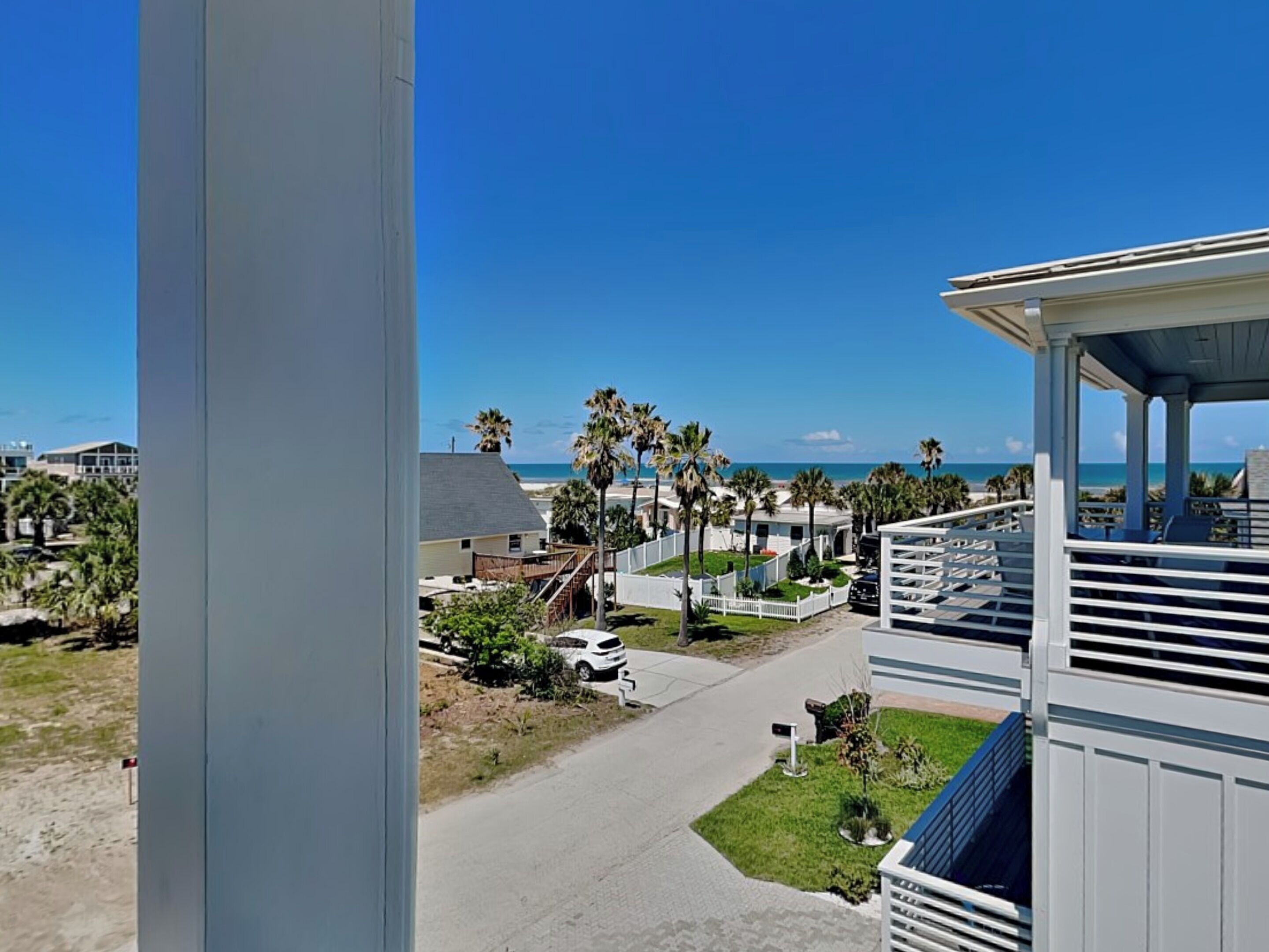 A beachfront property with a covered patio, a pathway leading to the beach, and palm trees.