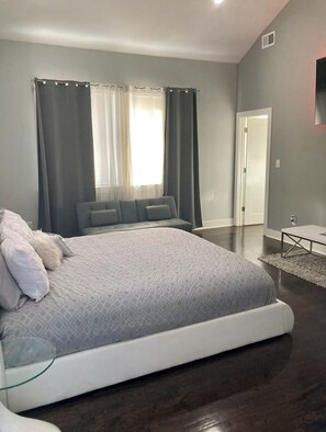 Ein Schlafzimmer mit einem großen Bett, grauen Vorhängen, einer weißen Tür und einem kleinen Tisch.