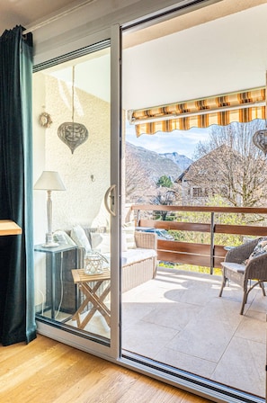 Ein Zimmer mit einer Schiebeglastür, die auf einen Balkon mit Korbmöbeln und Bergblick führt.