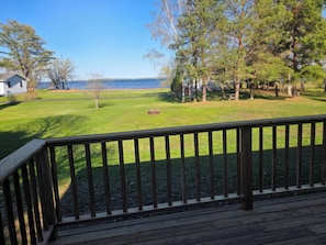 Une terrasse en bois avec une balustrade, une pelouse, des arbres et une étendue d’eau en arrière-plan.