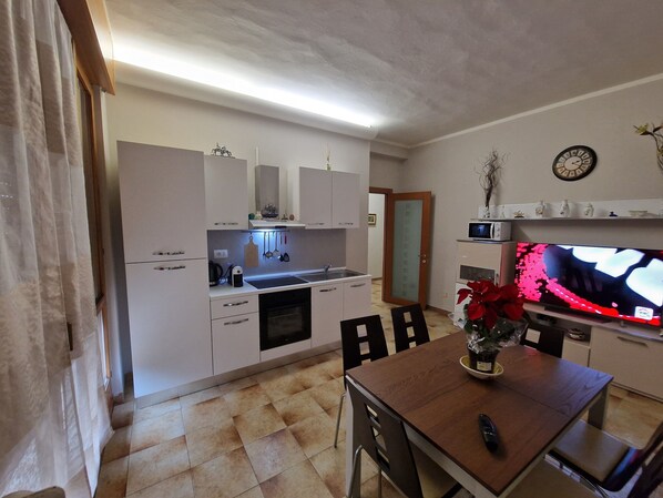 A compact kitchen with white cabinets, a microwave, a TV, and a dining area with a table and chairs.