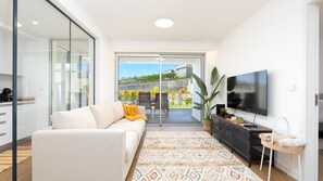 Ein modernes Wohnzimmer mit Sofa, Fernseher und Blick auf einen Garten durch Glastüren.