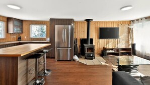 Une cuisine moderne dotée d’un îlot central, d’appareils électroménagers en acier inoxydable, d’un poêle à bois et d’un téléviseur à écran plat.