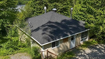 A small, single-story building with a dark roof, surrounded by dense green foliage and a body of water in the background.