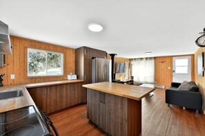 A modern kitchen with wooden cabinets, a central island, and a dining area with a sofa. - Chalet Bellevue au Lac du Cœur (Saint-Adolphe-d`Howard)