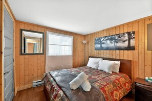 A bedroom with wooden walls, a bed with patterned bedding, a window, and a painting of a tree. - Chalet Bellevue au Lac du Cœur (Saint-Adolphe-d`Howard)