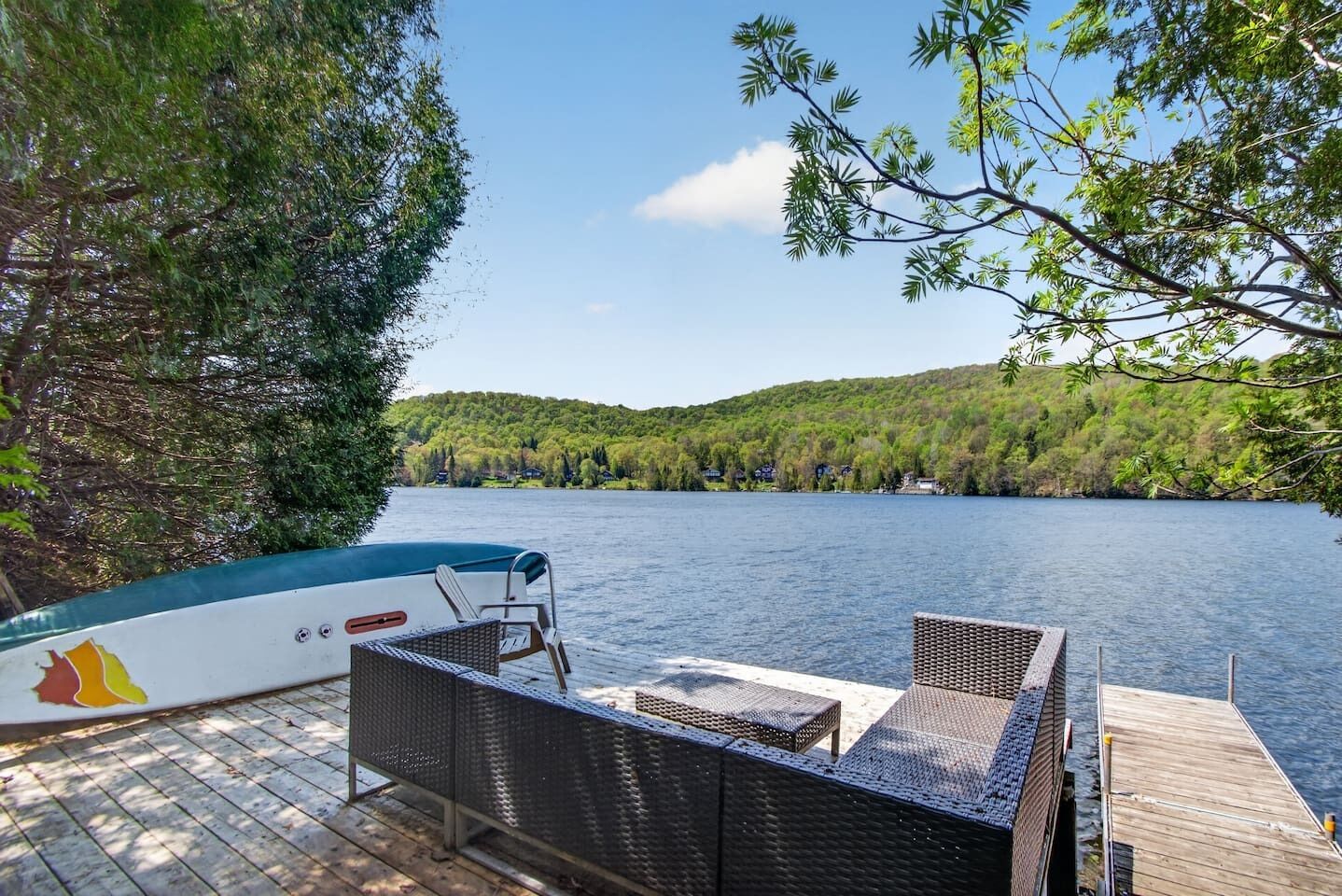 Une jetée avec un bateau, des meubles en osier et une vue sur un lac entouré d’arbres.