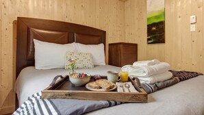 Une chambre d’hôtel avec une tête de lit en bois, un lit avec une literie blanche, un plateau avec des articles pour le petit-déjeuner et un tableau accroché au mur.