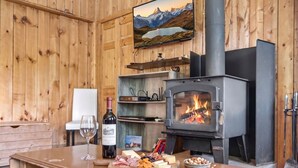 Un intérieur en bois avec une cheminée, une bouteille de vin, du fromage et un livre posés sur une table.
