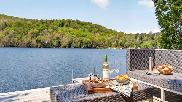 Un espace de restauration au bord du lac, avec des meubles en osier, une bouteille de vin, des verres et un bol de collations.