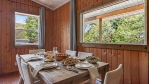 Un coin repas avec une table en bois dressée pour quatre personnes, entouré de murs en bois et de grandes fenêtres.
