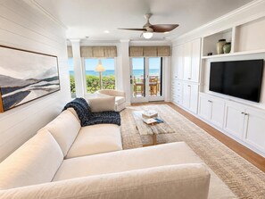 Ein Wohnzimmer mit einer Couch, einem Couchtisch, einem Fernseher und Blick ins Freie.