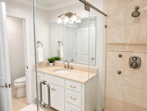 Un baño moderno con cabina de ducha de vidrio, un lavabo con espejo y un inodoro visible a través de la puerta de cristal.