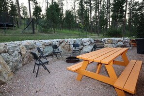 An outdoor seating area with a stone wall, picnic table, and chairs. - Eagles Nest Cabin, full kitchen, cover carport, Restmore Inn, Hill City (Hill City)