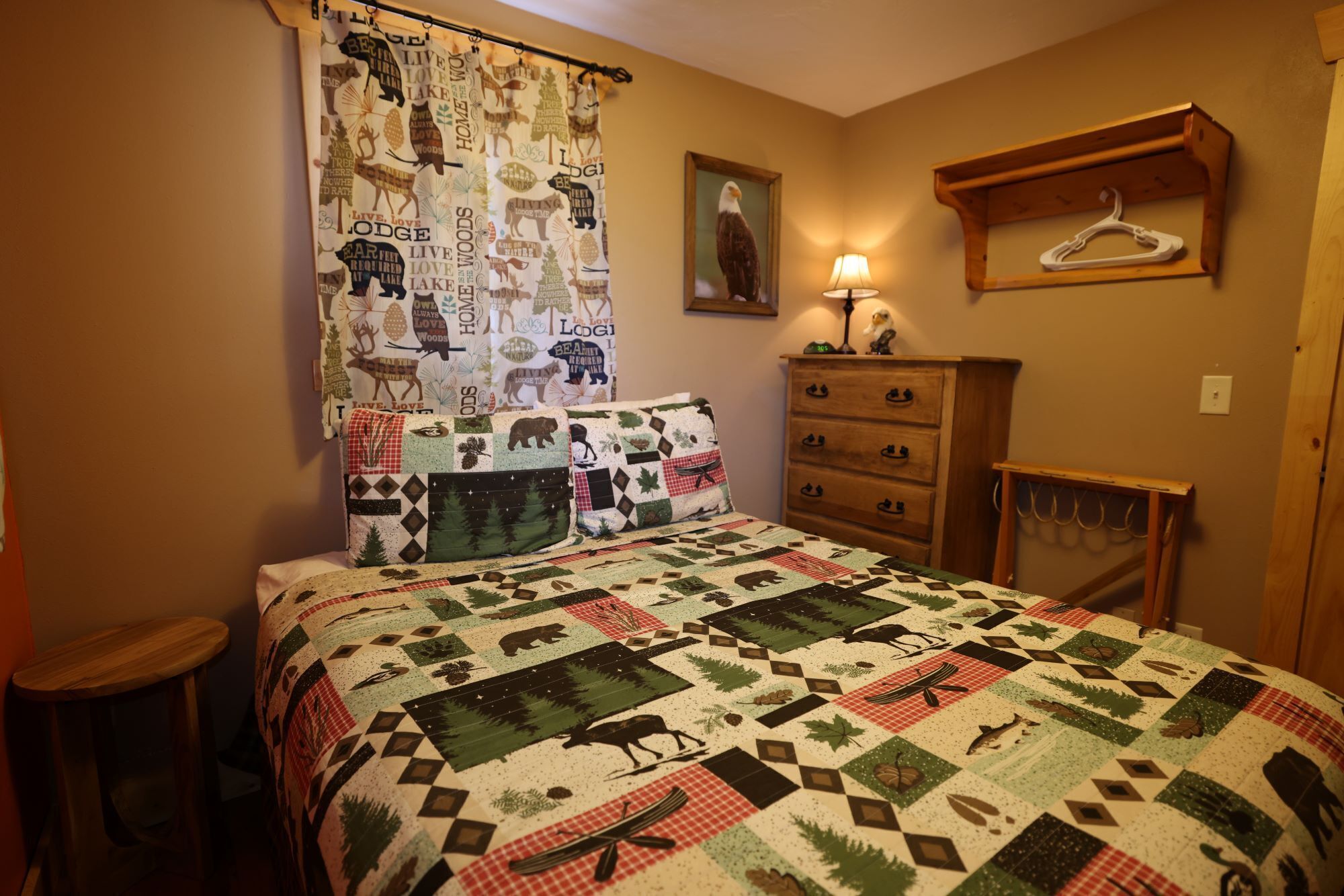A bedroom with a bed, a dresser, a lamp, a coat rack, and a curtain with animal prints.