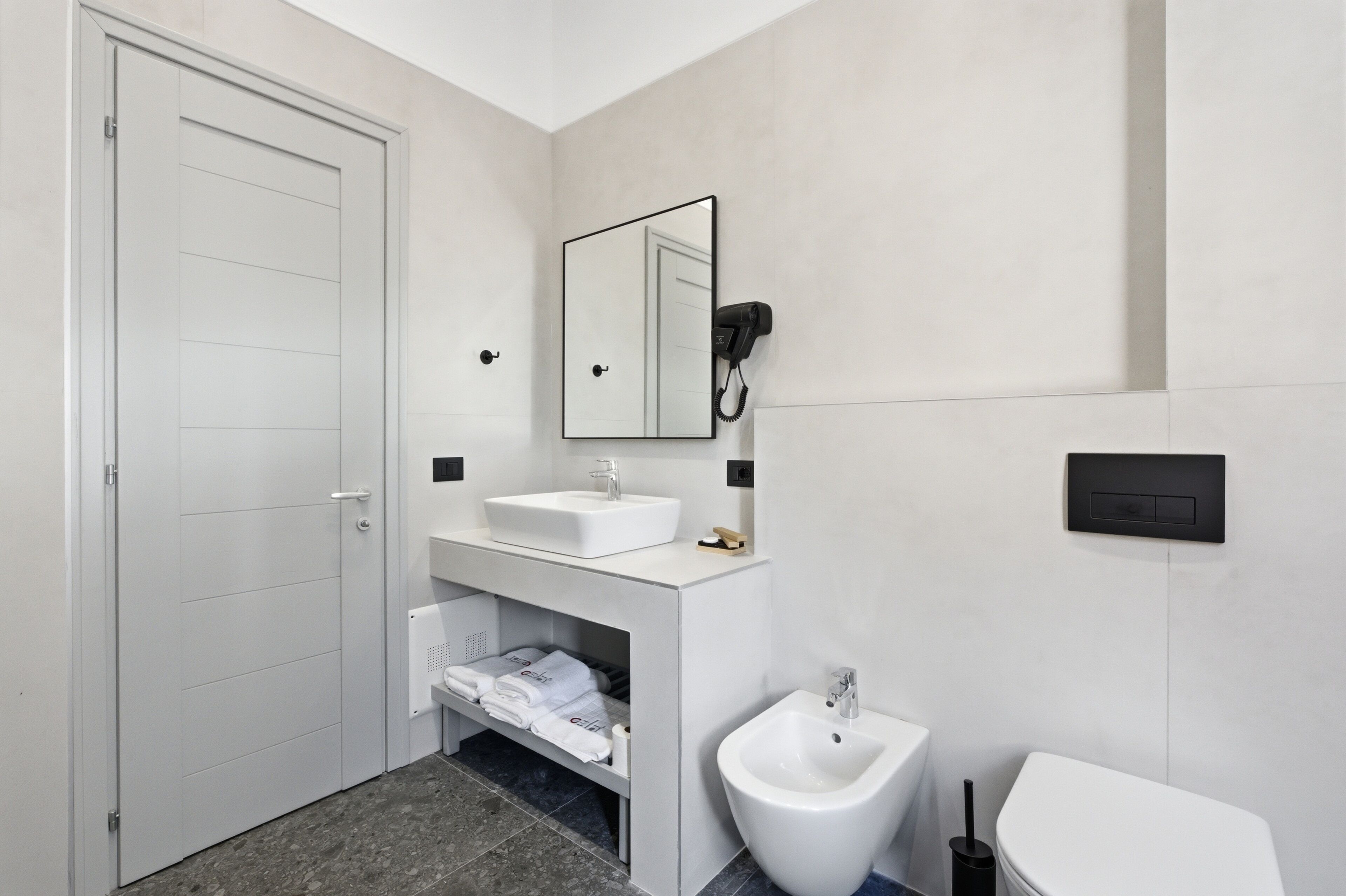 A modern bathroom with a white door, a white sink, a bidet, and a toilet.