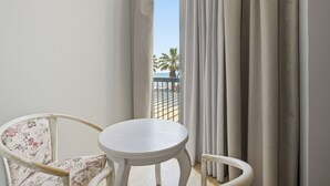 A balcony with a white table and floral chair, curtains, and a view of palm trees and a building. - Cela Hotel (Durrës)
