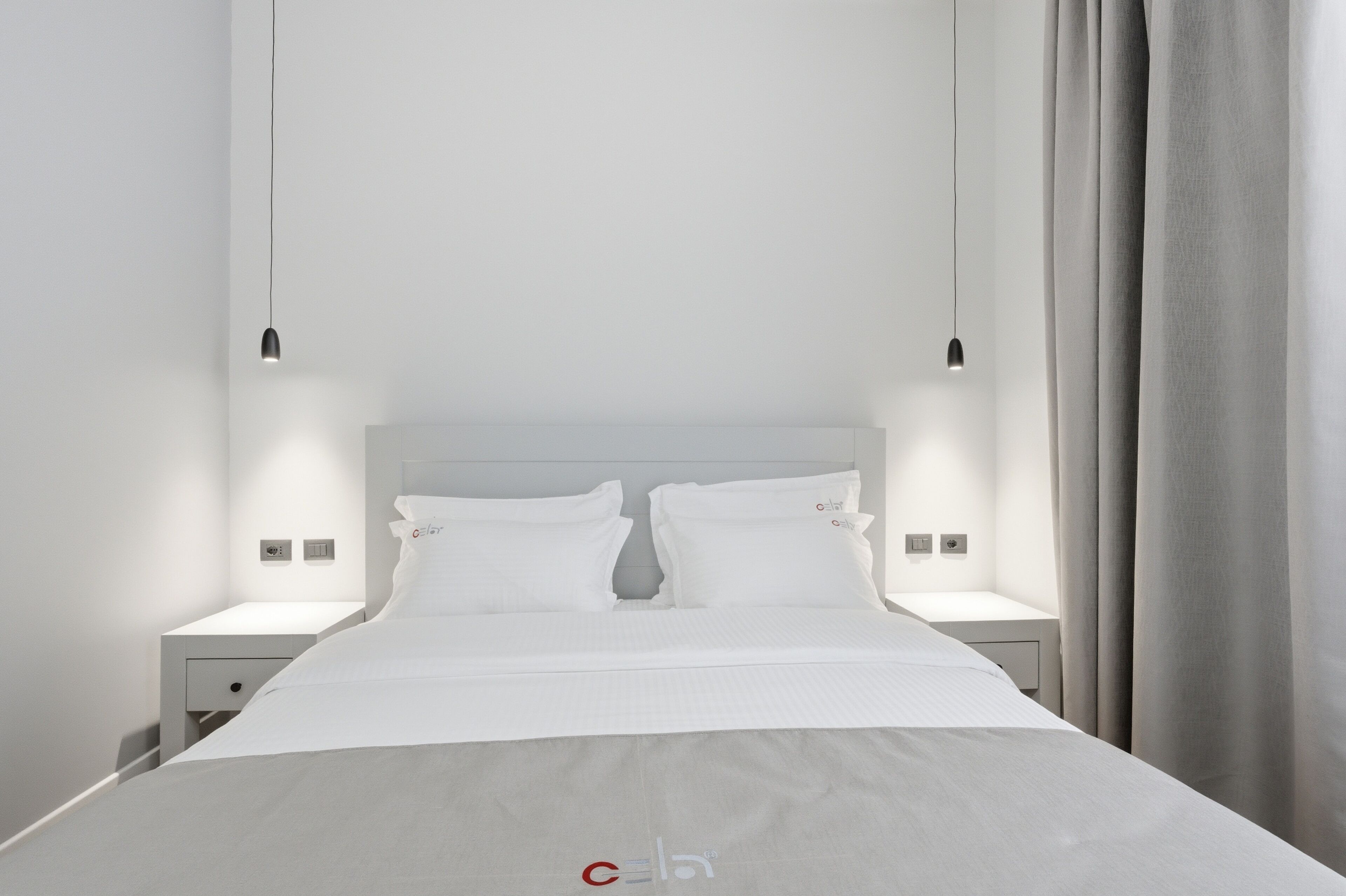 A modern hotel room with a large bed, two bedside tables, and a hanging light fixture.