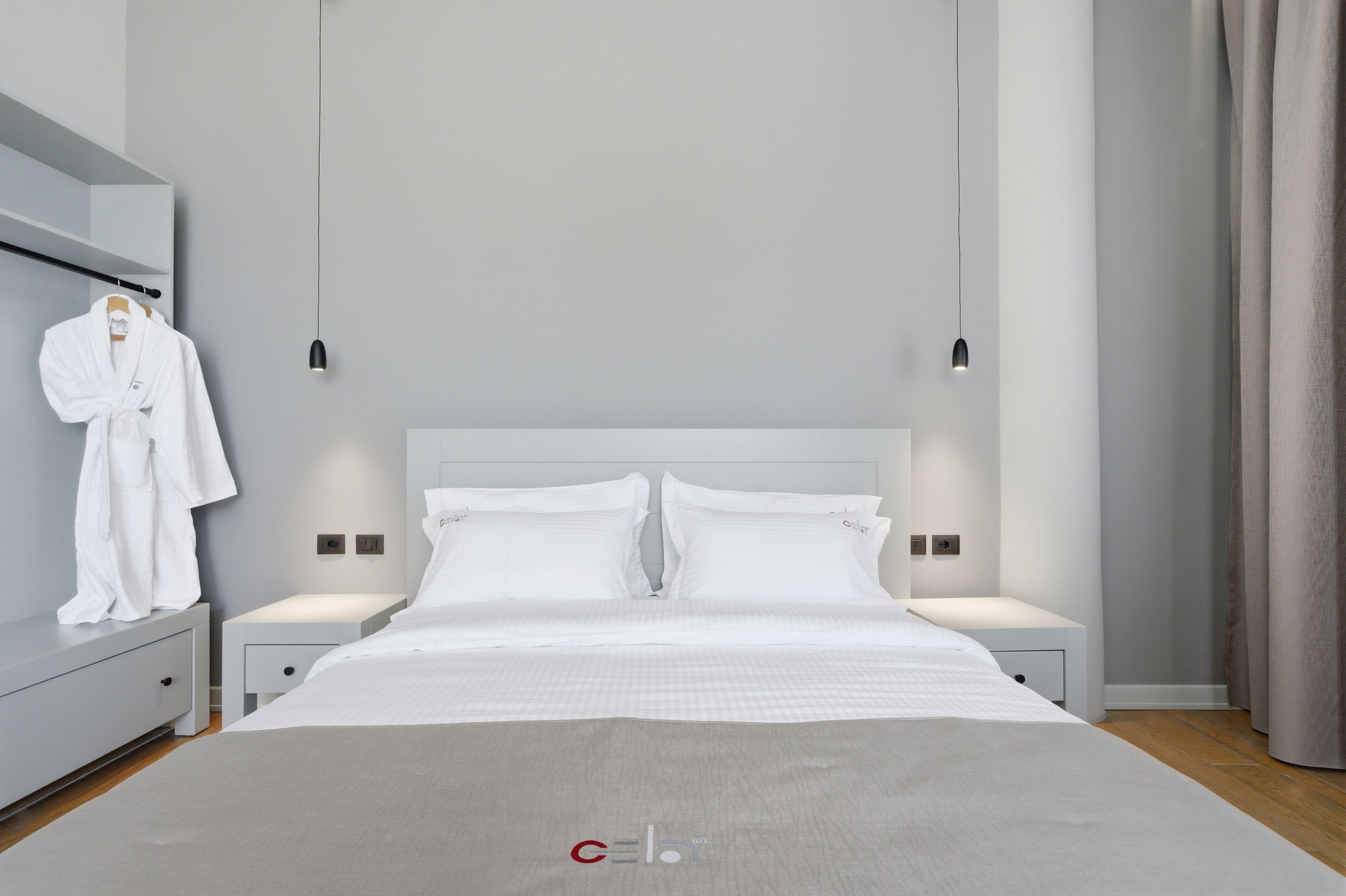 Una habitación de hotel moderna con una cama grande, mesitas de noche, un armario y una bata colgada.