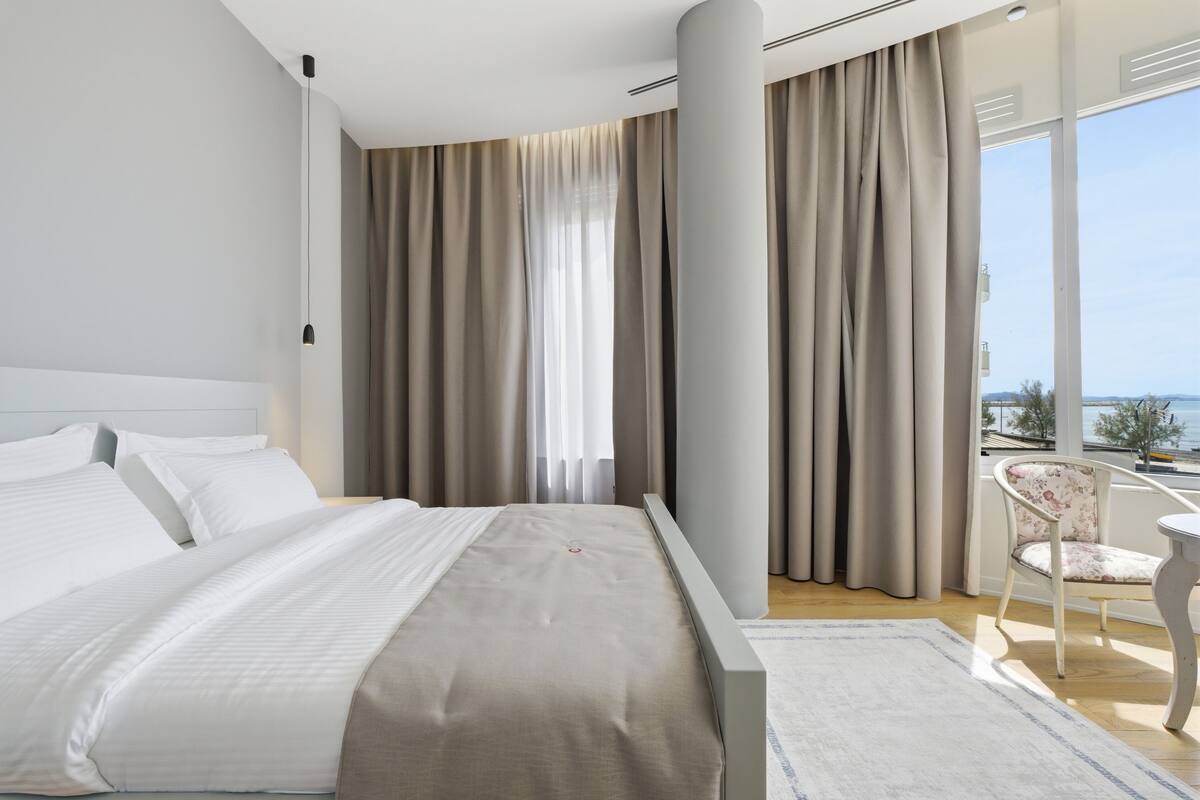 Una habitación de hotel moderna con una cama grande, vista al mar y un balcón con una silla.