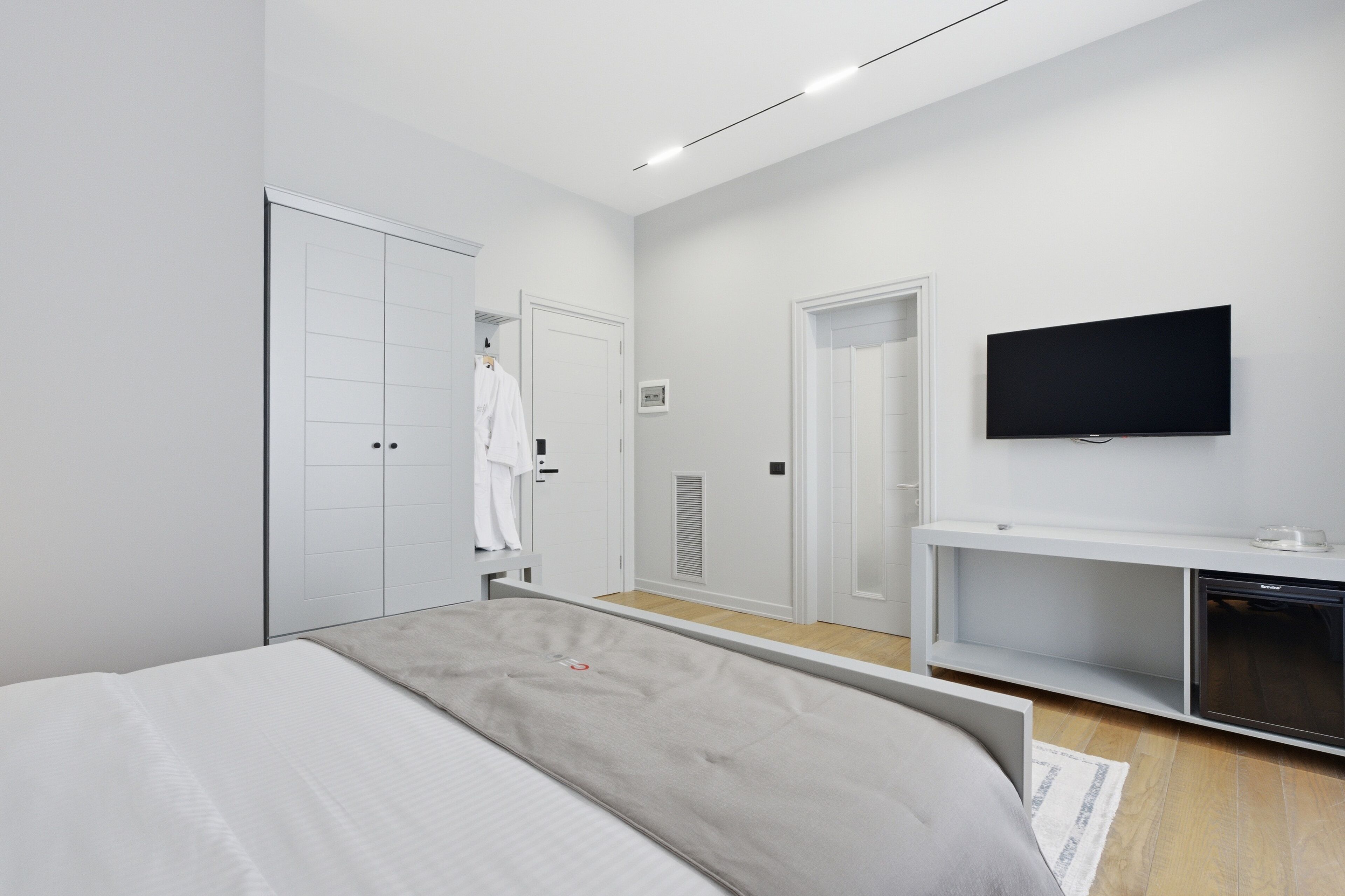 A modern bedroom with a bed, a TV, a wardrobe, and a console table.