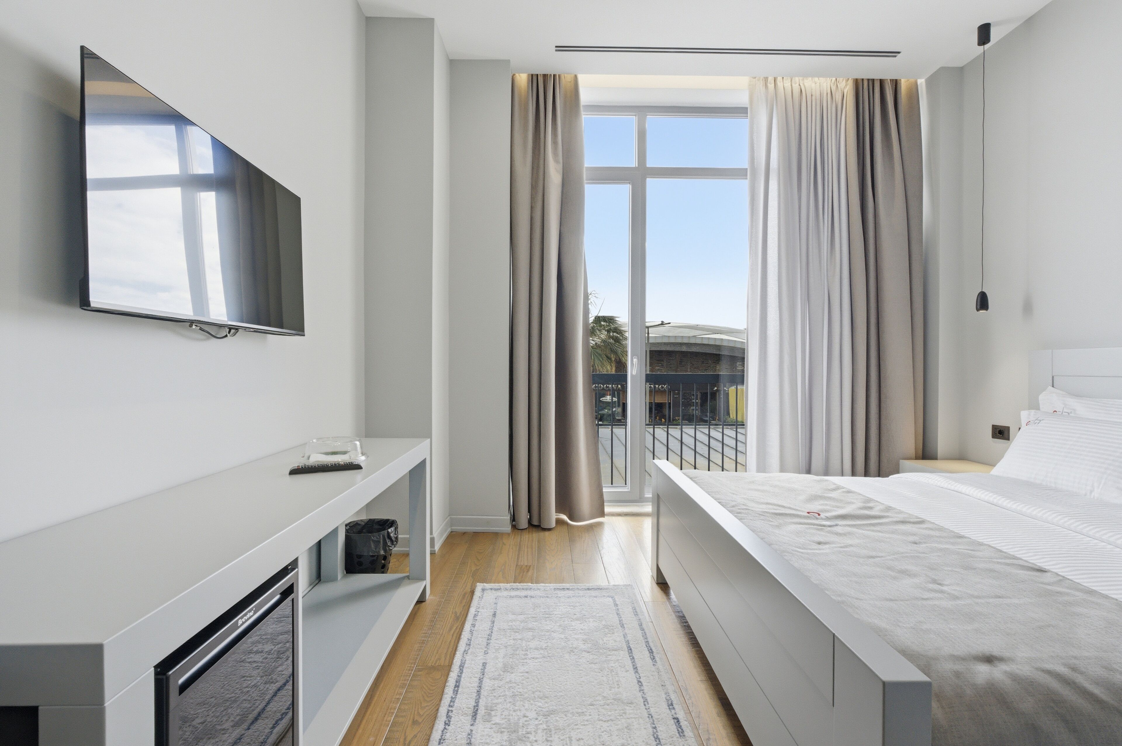 Una habitación de hotel moderna con televisión de pantalla plana, una cama, un escritorio y una ventana con cortinas.