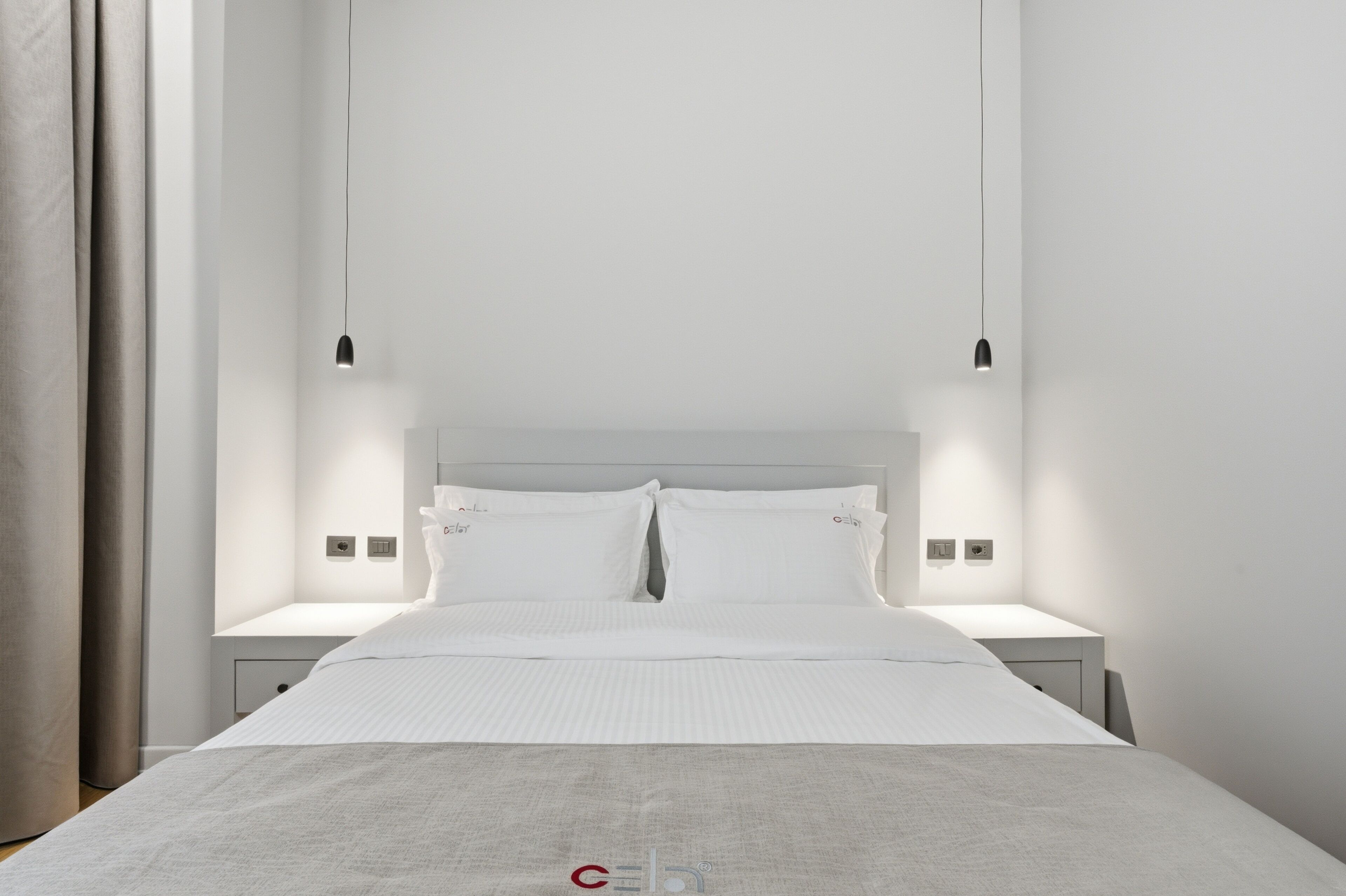 A modern hotel room with a large bed, bedside tables, and pendant lighting.