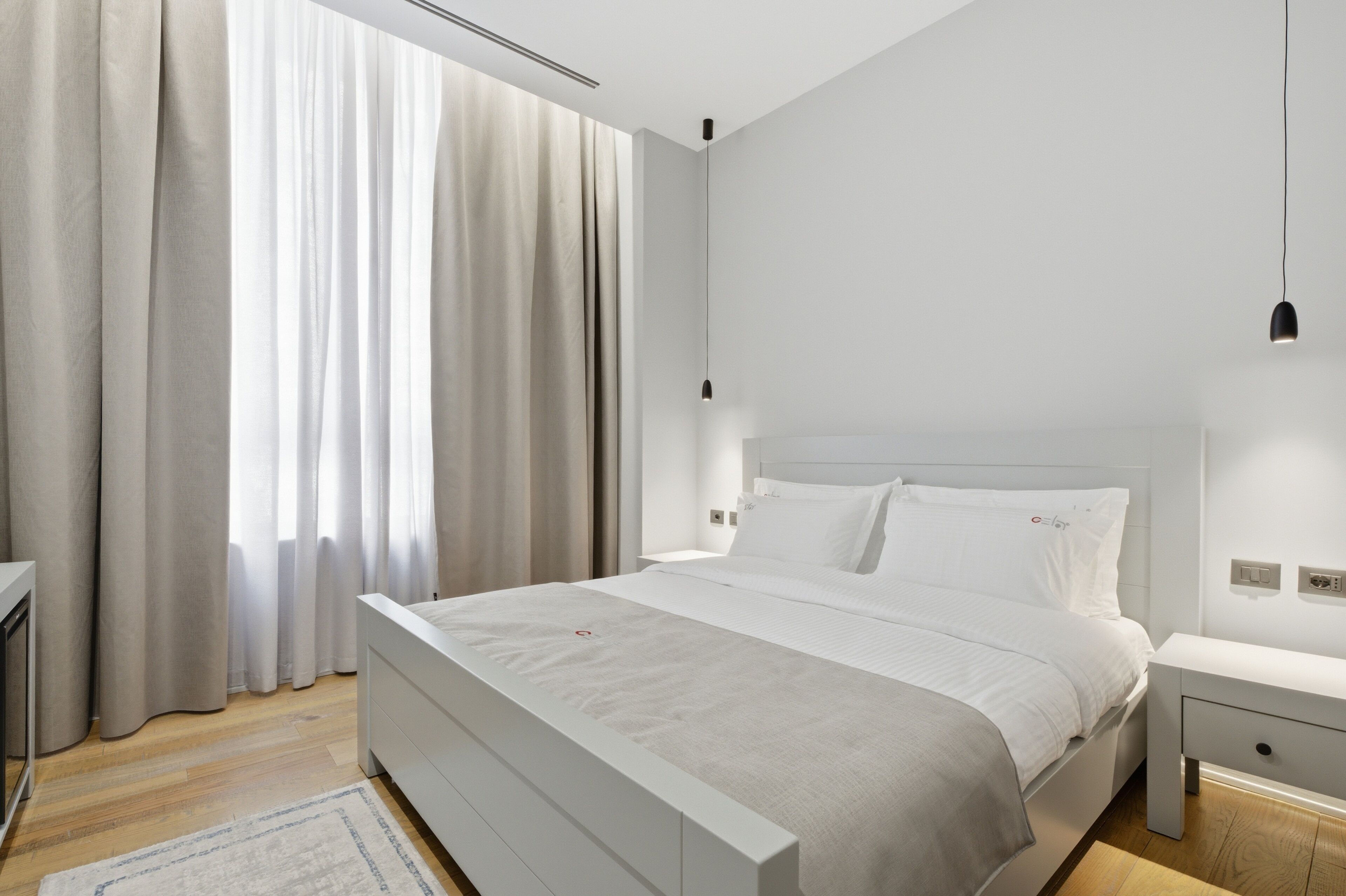 A modern bedroom with a large bed, bedside tables, and a window with curtains.