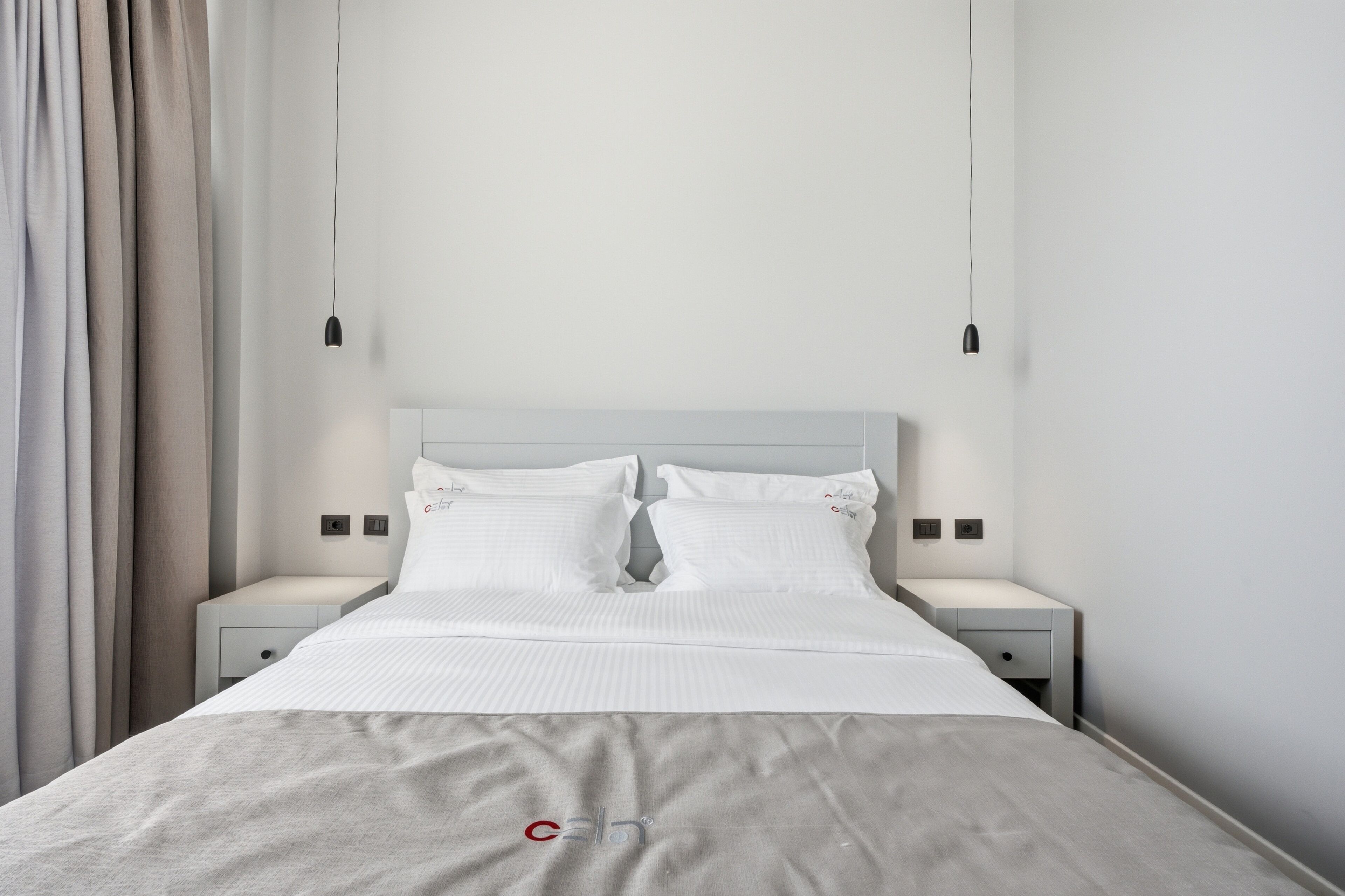 A neatly made bed with white linens, two bedside tables with lamps, and a curtain on the left.