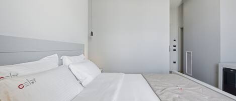 A modern hotel room with a large bed, a bedside table, a wall-mounted heater, and a door leading to a bathroom.