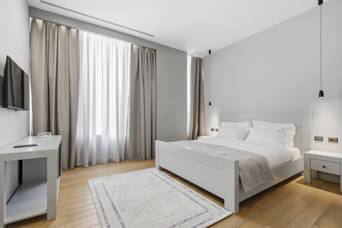 Un dormitorio moderno con una cama, mesitas de noche, un televisor y cortinas.