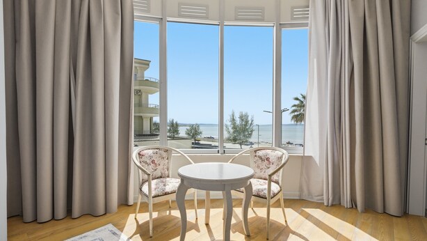 A room with a large window, two chairs, a round table, and a wooden floor. - Cela Hotel (Durrës)
