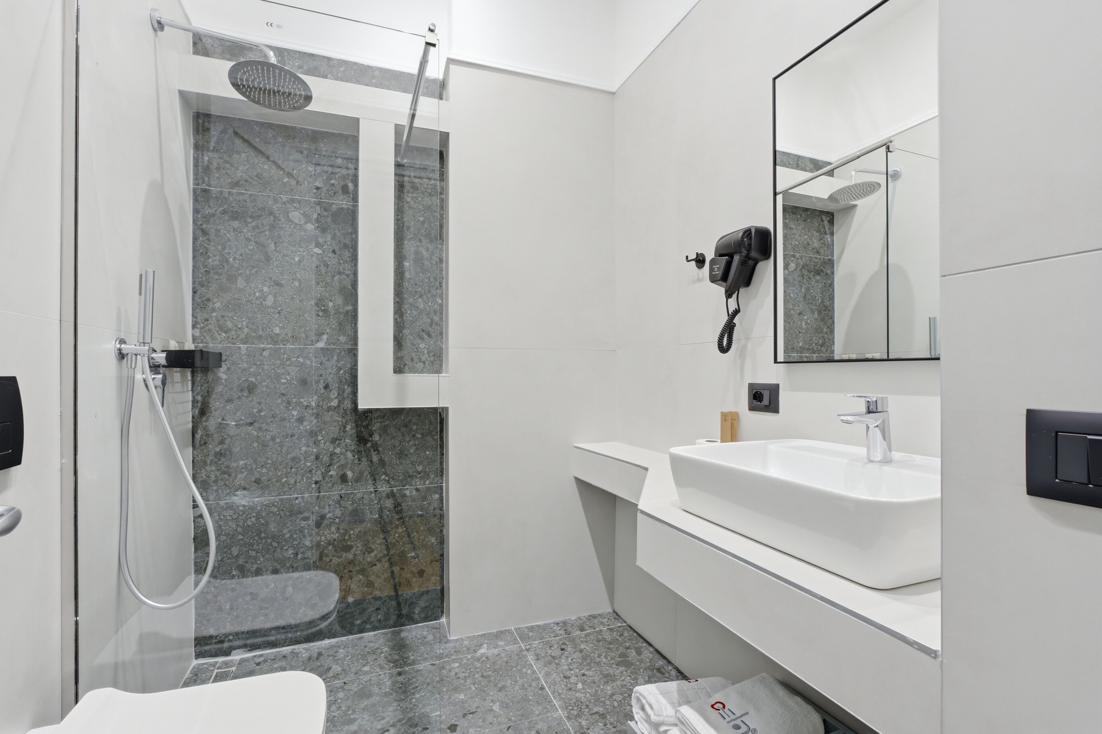 A modern bathroom with a glass-enclosed shower, a white sink, and a hairdryer mounted on the wall.