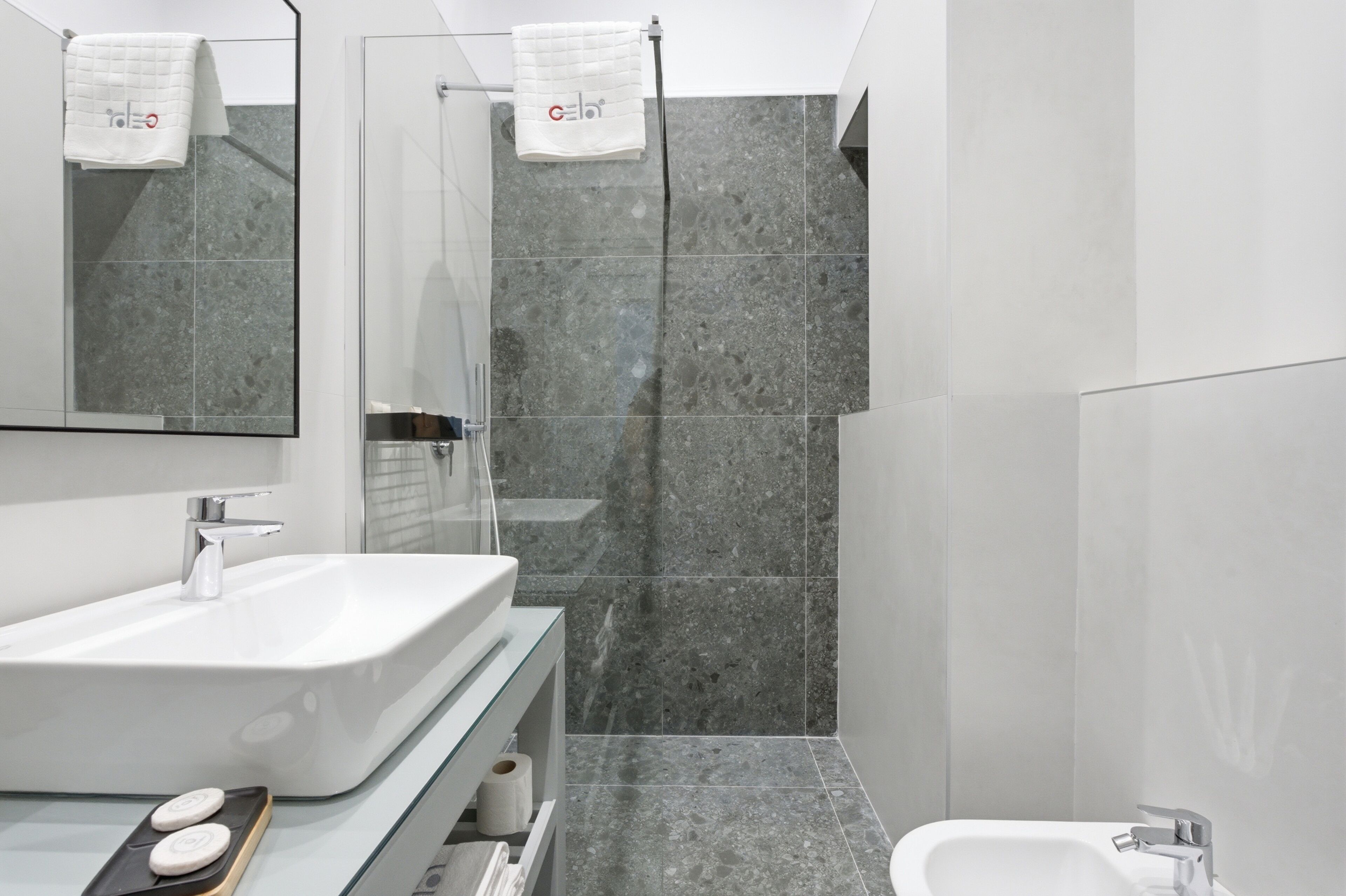 A modern bathroom with a large mirror, a white sink, a shower, and a toilet.