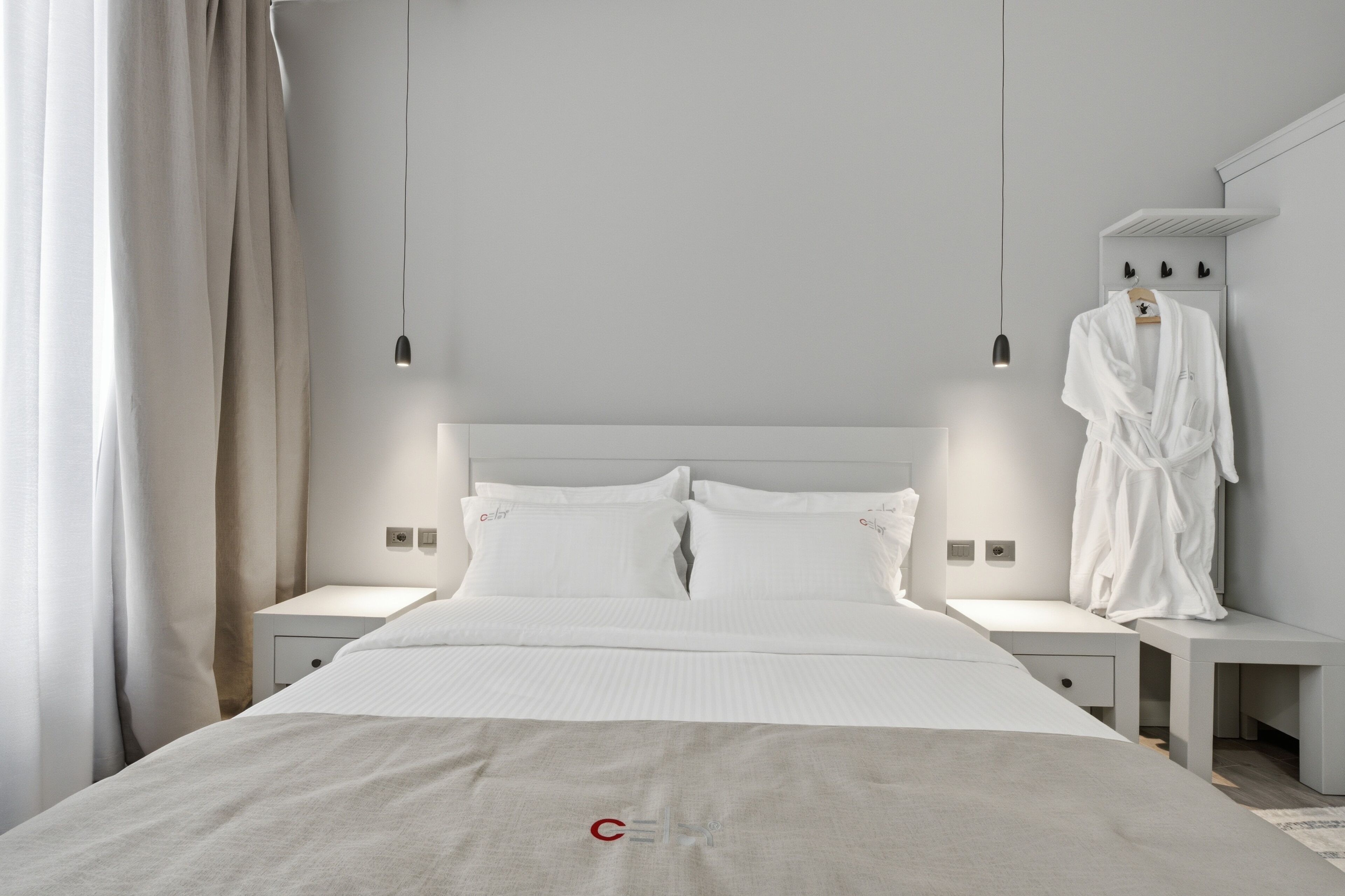 A modern hotel room with a large bed, bedside tables, a robe rack, and a hanging light fixture.