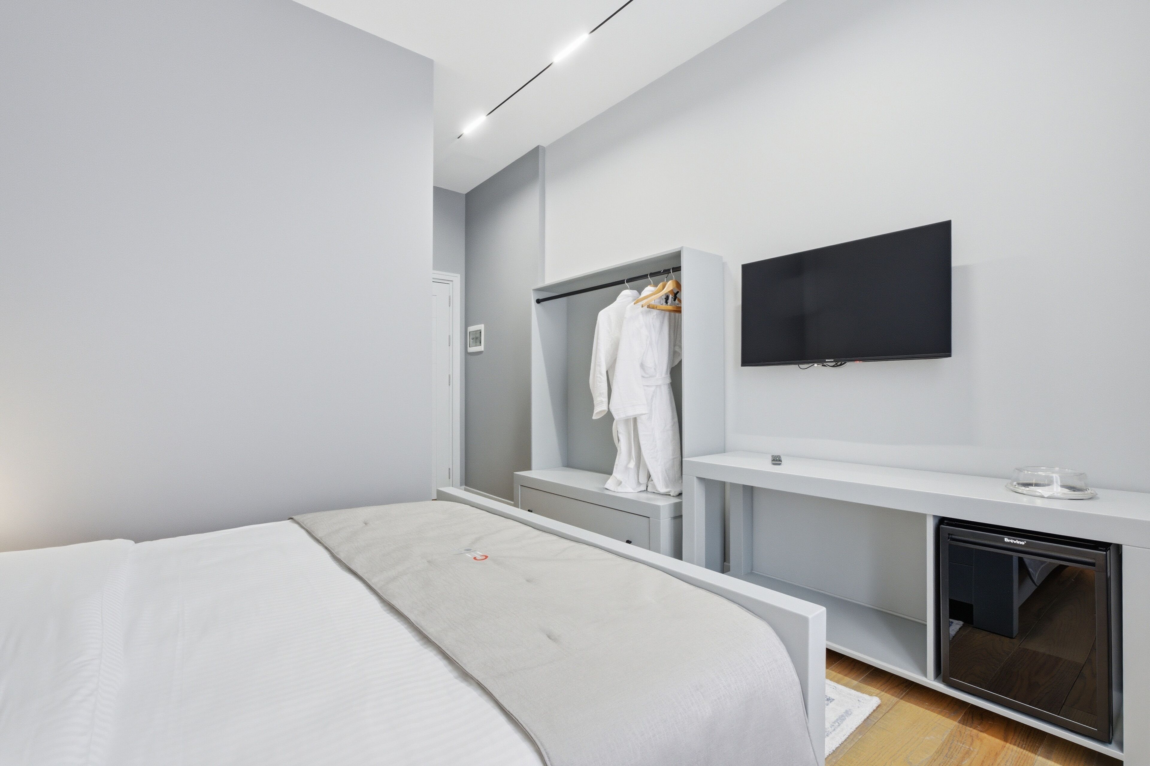 A modern hotel room with a bed, a wardrobe, a TV, and a mini-fridge.